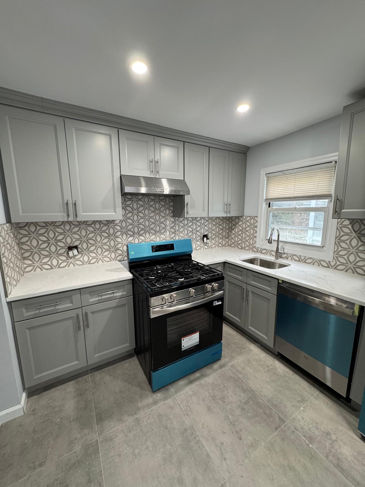 Gray kitchen cabinets with patterned backsplash and new flooring.